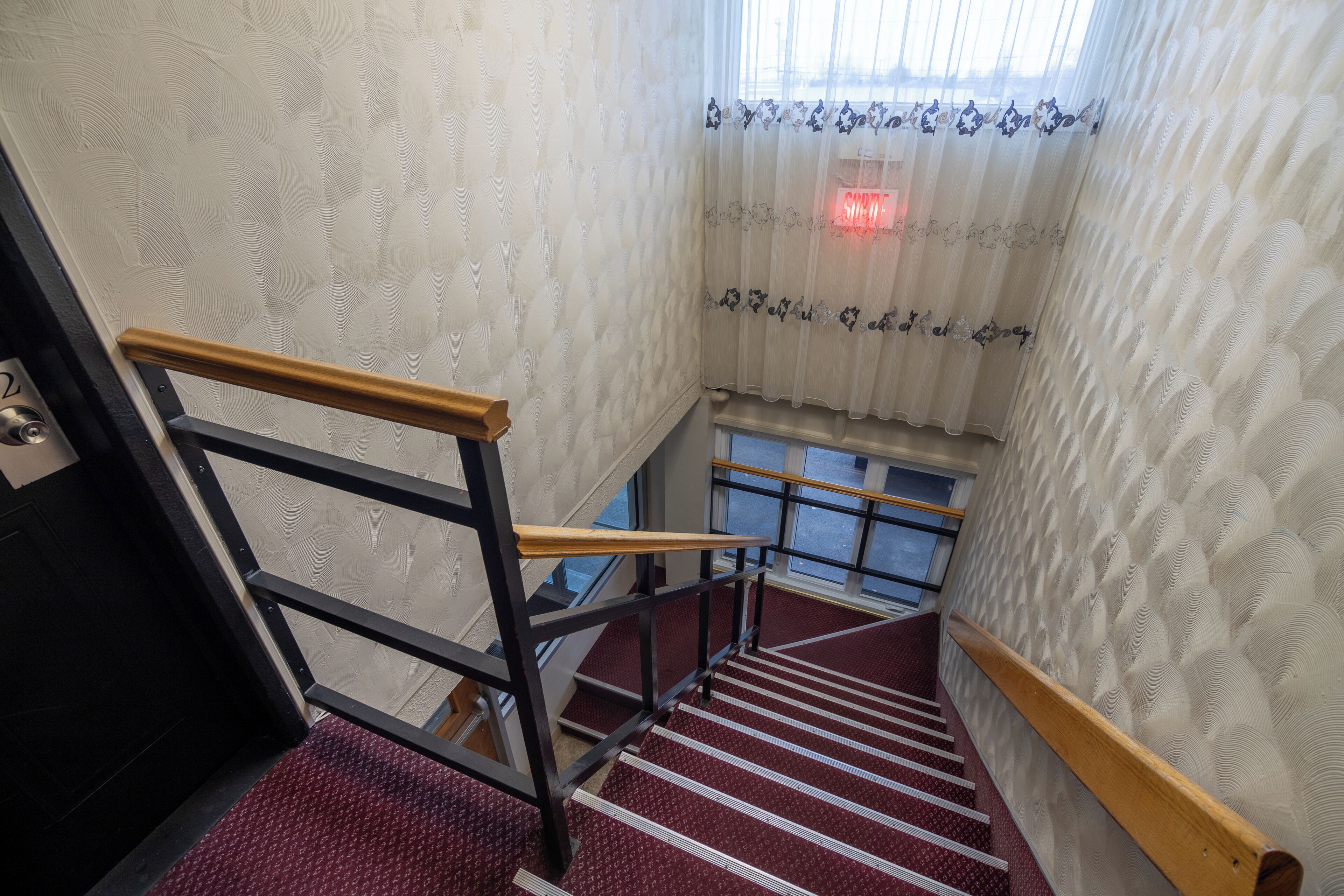 Eine Treppe mit einer Holzhandläufe und einem roten Teppichboden, die zu einer Ebene mit einem Fenster und einer verschlossenen Tür führt.