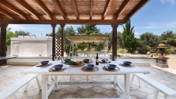 Un espace extérieur aménagé pour les repas, avec une pergola en bois, une table blanche et des bancs.
