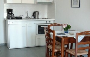 A compact kitchen with white cabinets, a stove, a coffee maker, and a dining table with chairs.