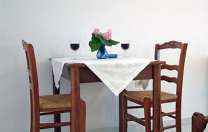 A dining table with a white tablecloth, two chairs, a vase with pink flowers, and two glasses of red wine.