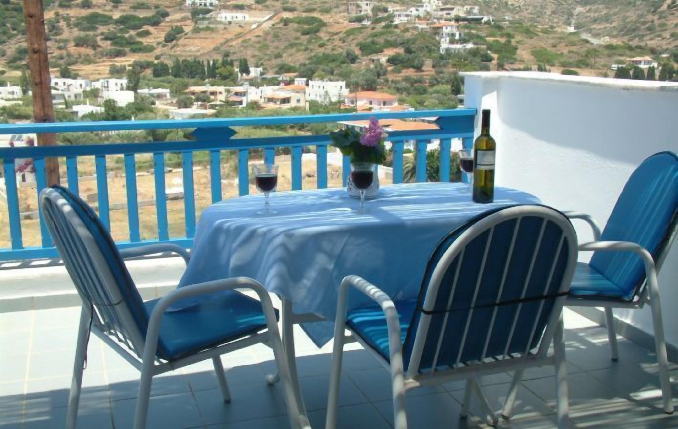 A terrace with a table set for two, a bottle of wine, and a vase with flowers.