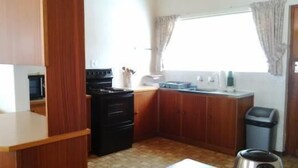 A compact kitchen with wooden cabinets, a black stove, and a window with curtains. - Holiday House Sedgefield (Sedgefield)