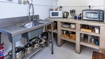 A compact kitchen with a stainless steel sink, a microwave, a toaster oven, and various utensils and cookware.