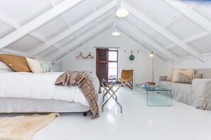 An attic bedroom with a bed, a glass coffee table, a sofa, and a hanging light fixture. - SaWestCoast & Beyond (Paternoster)