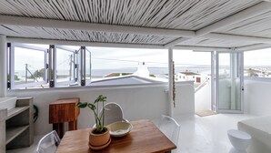 A modern interior with a wooden table, potted plants, and a view of the sea through large windows. - SaWestCoast & Beyond (Paternoster)