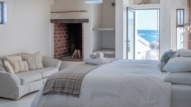 A bedroom with a large bed, a sofa, a fireplace, and a view of the sea. - SaWestCoast & Beyond (Paternoster)