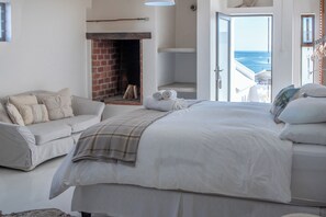A bedroom with a large bed, a sofa, a fireplace, and a view of the sea. - SaWestCoast & Beyond (Paternoster)