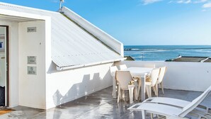A sunlit outdoor seating area with a table and chairs, a lounge chair, and a view of the ocean. - SaWestCoast & Beyond (Paternoster)
