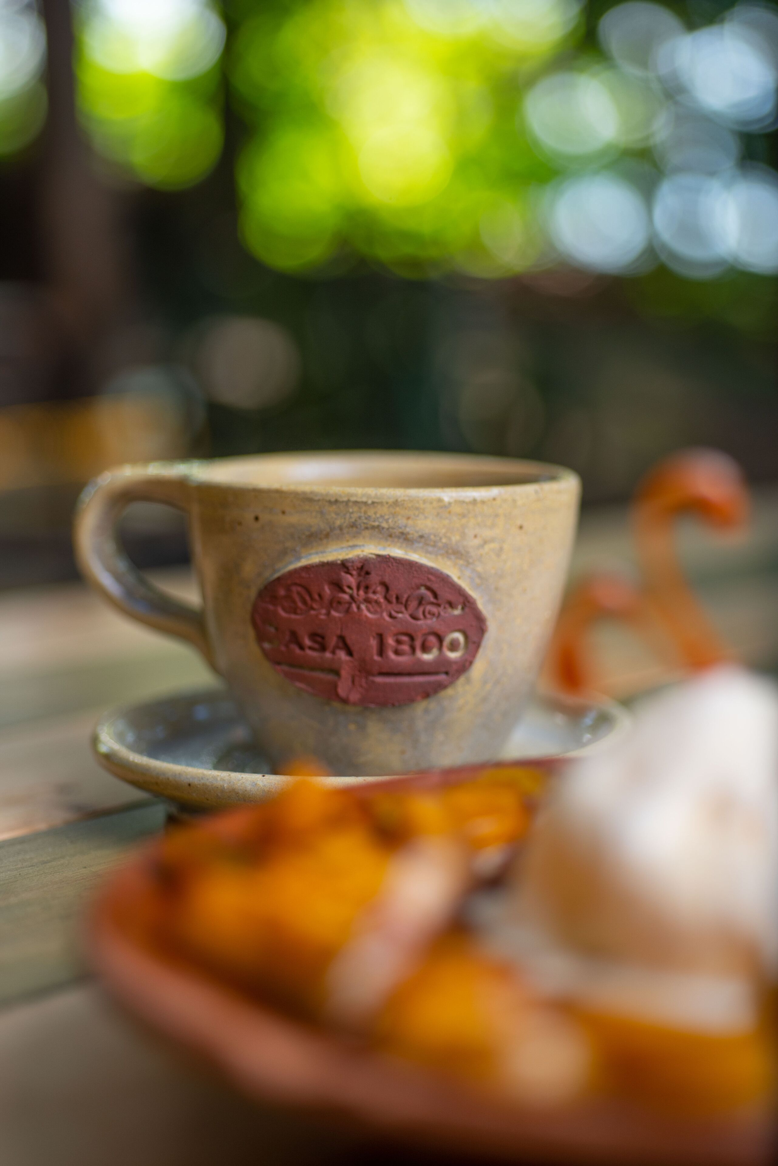 A ceramic cup with an embossed logo and a saucer on a wooden table.