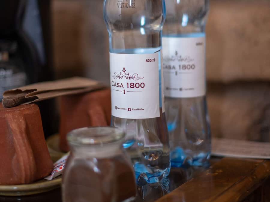 Dos botellas de agua con la etiqueta "Casa 1800" sobre una mesa de madera con un fondo de pared de ladrillo.