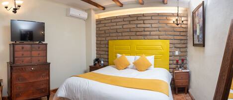 Una habitación de hotel con pared de ladrillo, cabecera amarilla, televisor de pantalla plana, muebles de madera y candelabro.