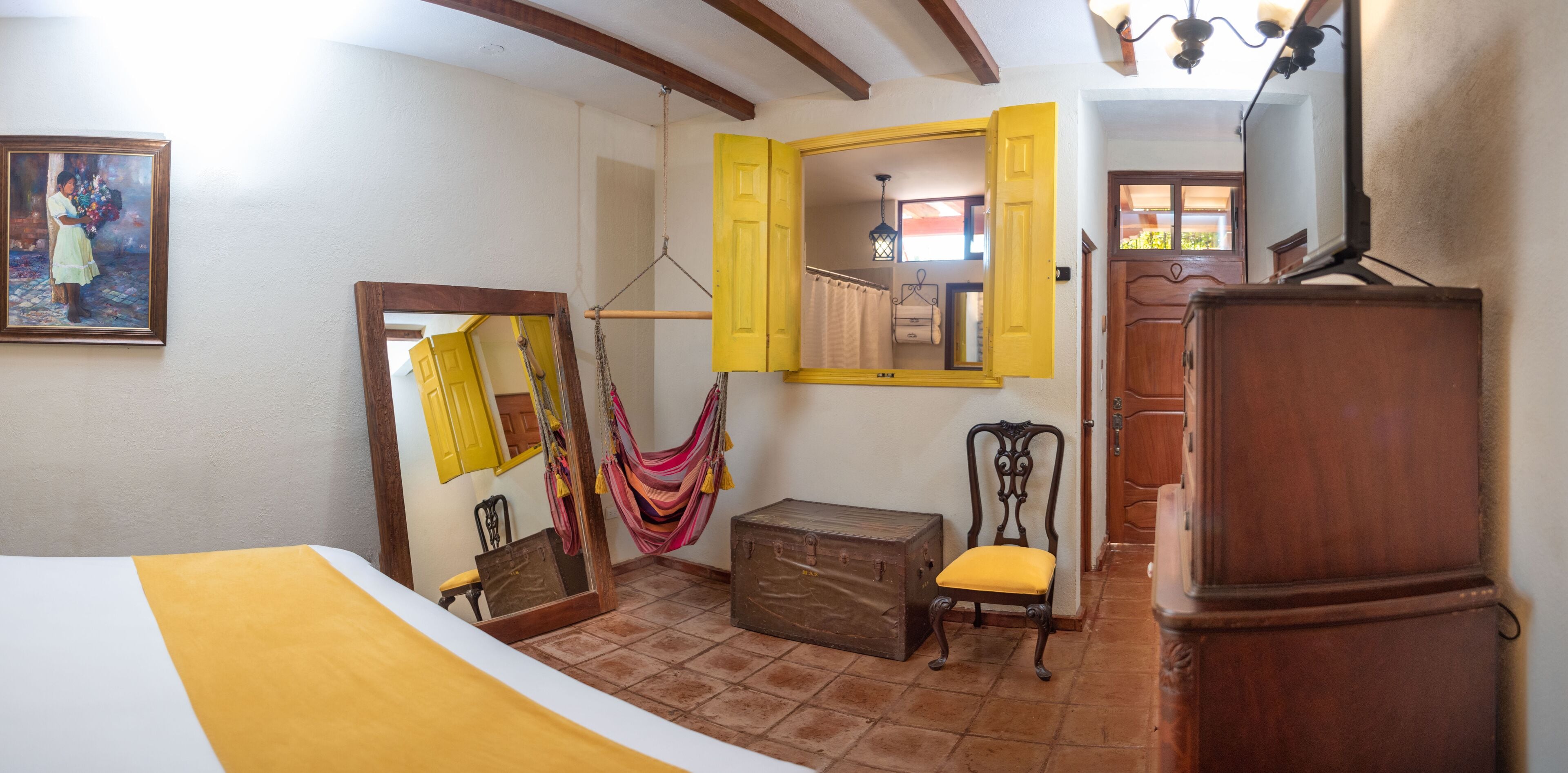 A room with a bed, a chair, a suitcase, a hammock, and a wooden cabinet.