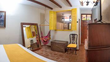 A room with a bed, a chair, a suitcase, a hammock, and a wooden cabinet.