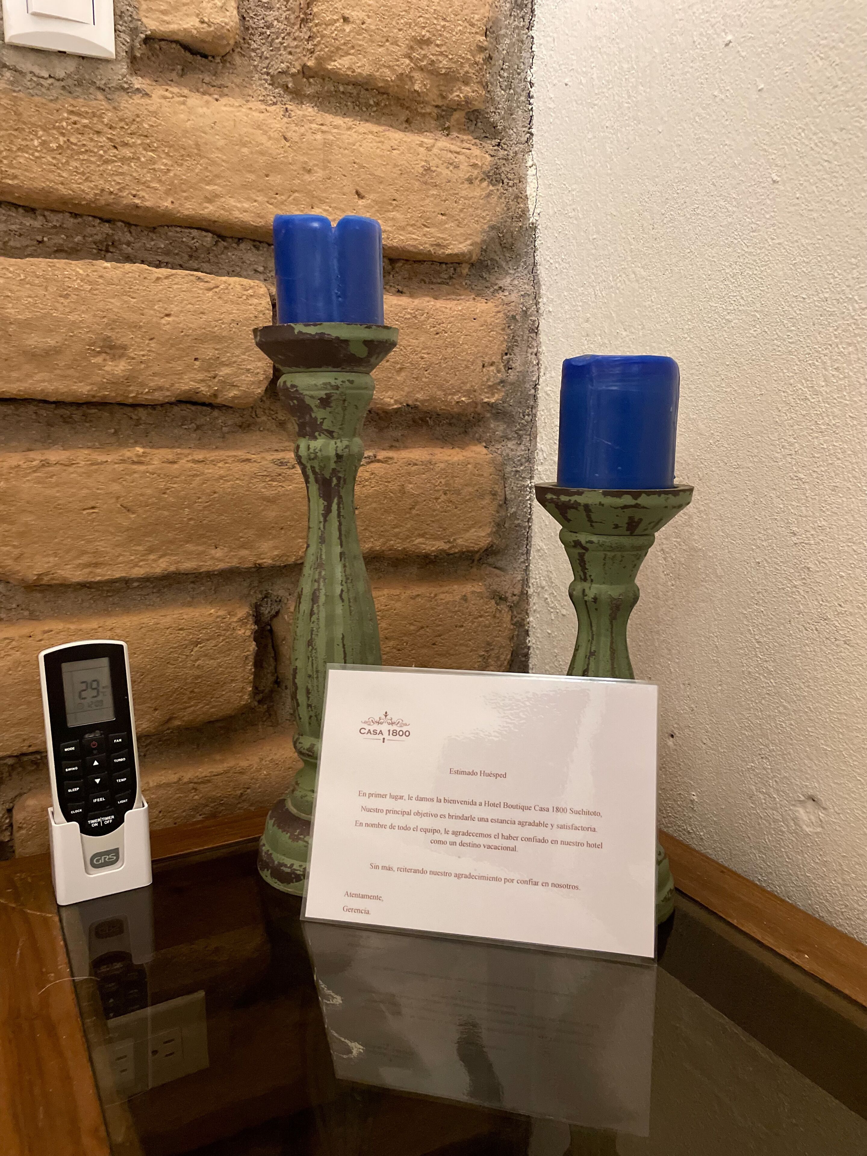 Une enseigne d’hôtel avec un message en espagnol, deux chandeliers de style ancien avec des bougies bleues, et un appareil numérique posé sur une table.