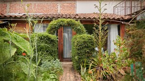 A rustic house with a brick facade, a tiled roof, and a small garden with various plants and a pathway leading to the entrance. - Sereno Hotel (San Cristóbal de las Casas)