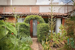 A rustic house with a brick facade, a tiled roof, and a small garden with various plants and a pathway leading to the entrance. - Sereno Hotel (San Cristóbal de las Casas)