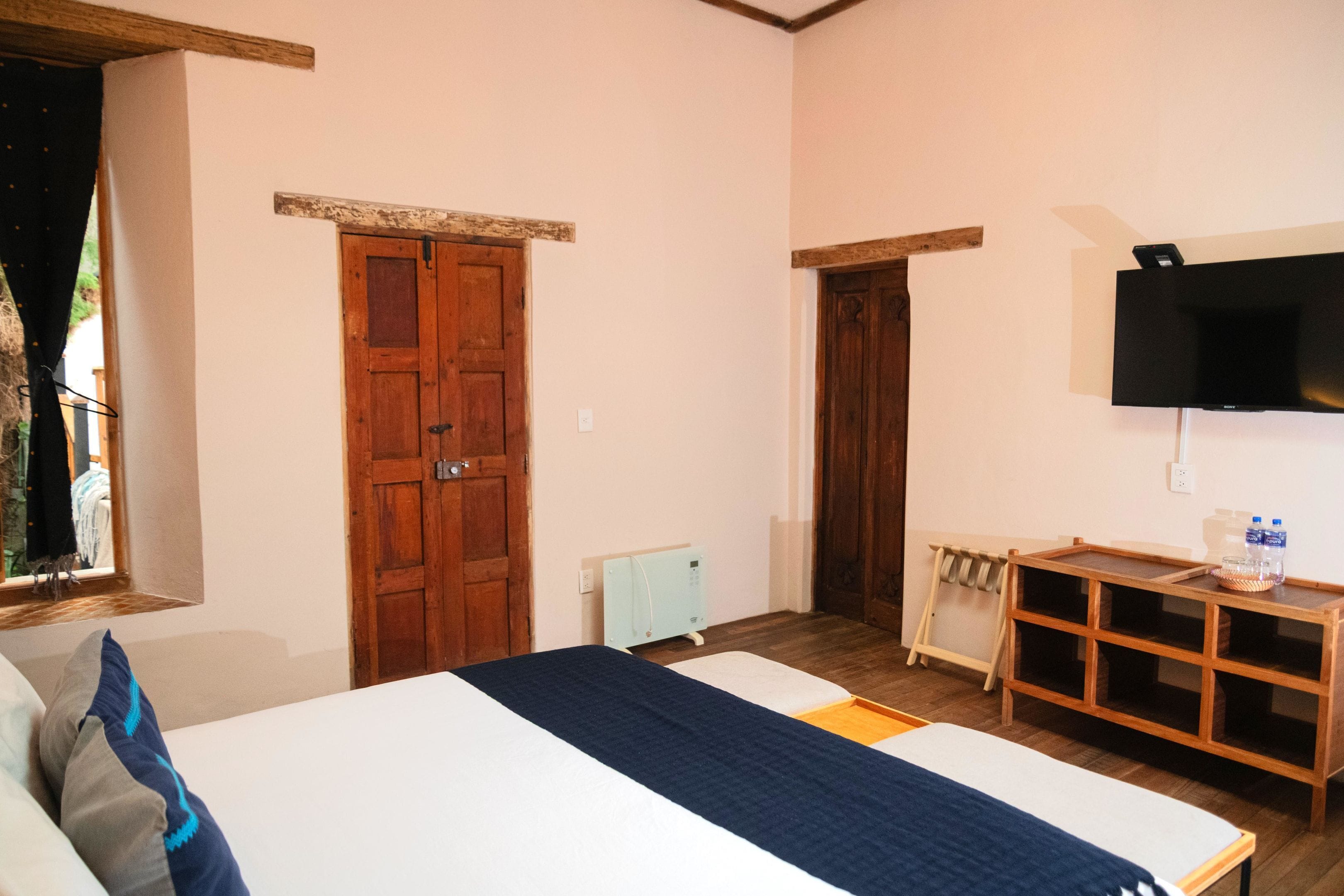 A bedroom with a bed, wooden wardrobe, a television, and a small table with a tray.