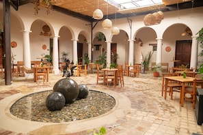 A spacious courtyard with a central water feature, surrounded by wooden tables and chairs, and adorned with hanging wicker lamps. - Sereno Hotel (San Cristóbal de las Casas)