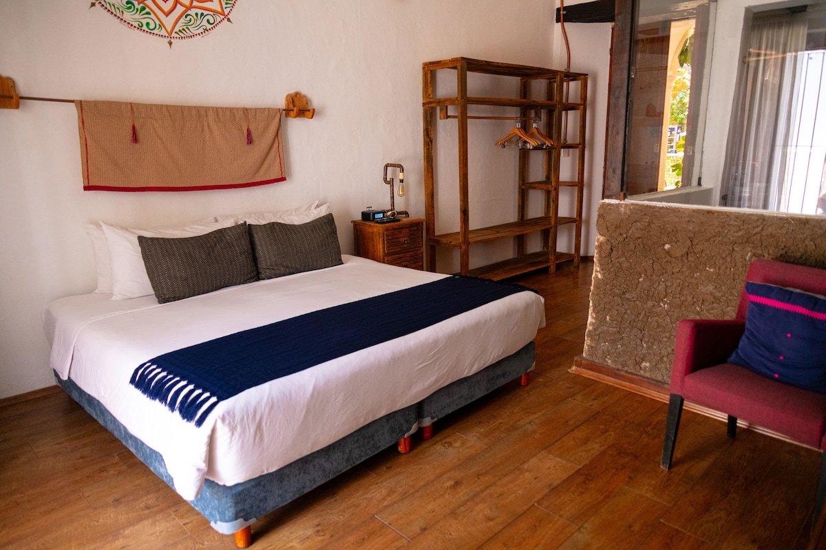 Quarto com cama grande, mesa de cabeceira de madeira, cabideiro e uma cadeira.