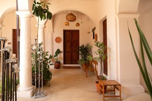 A hallway with white columns, wooden doors, and potted plants. - Sereno Hotel (San Cristóbal de las Casas)