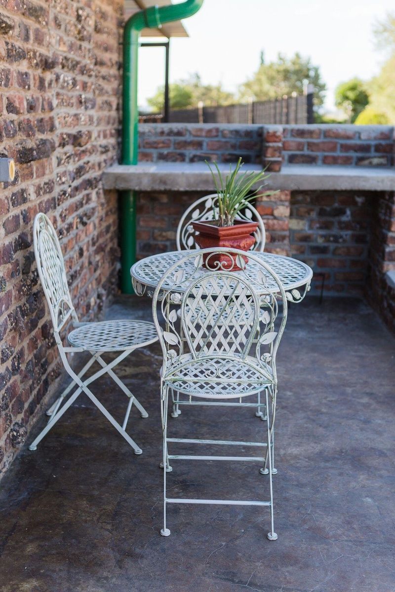 A metal outdoor table with chairs, a potted plant, and a brick wall.