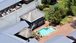 Una piscina en la azotea con una estructura de techo de paja, rodeada de un jardín ajardinado con palmeras y una piscina pequeña.