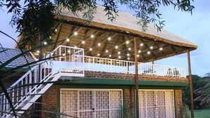 Un edificio de dos pisos con balcón cubierto, piscina y fachada de piedra.