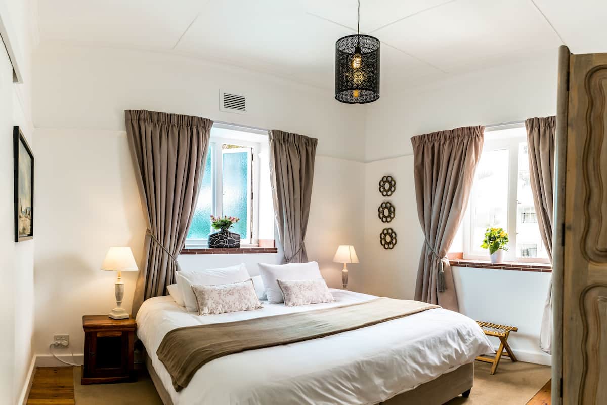 A bedroom with a large bed, two bedside tables, a hanging light fixture, and a window with curtains.