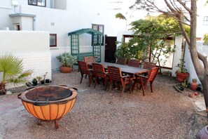 A patio with a table and chairs, surrounded by potted plants and a fire pit.