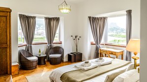 Une chambre d’hôtel avec un lit, deux fauteuils en osier, une petite table, une lampe et une vue sur l’extérieur.