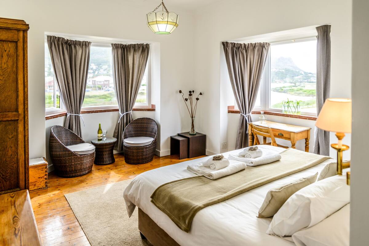 A hotel room with a bed, two wicker chairs, a small table, a lamp, and a view of the outdoors.