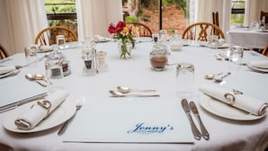 A neatly set dining table with white tablecloth, silverware, and a menu labeled "Jenny's Guest House". - Jenny's Guest House (Makhanda)