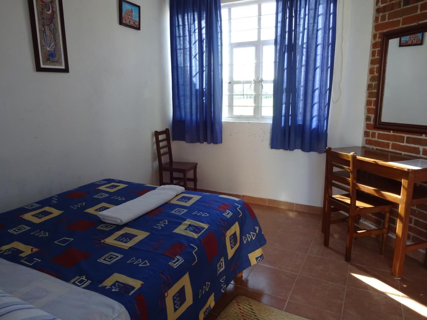 Un dormitorio con cama, una silla, un escritorio y una ventana con cortinas.