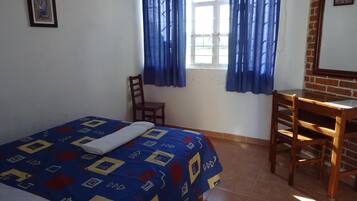 Un dormitorio con cama, una silla, un escritorio y una ventana con cortinas.
