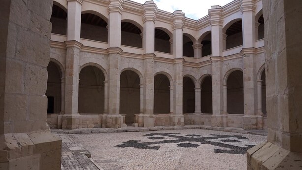 Un patio con un diseño geométrico de azulejos en el suelo, rodeado de columnas y arcos.