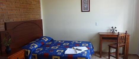 A bedroom with a bed, a wooden nightstand, a desk, and a chair.