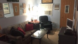 A living room with a sofa, armchair, coffee table, and a television on a stand. - Diamond in the Bluff (Pointe-du-Chene)