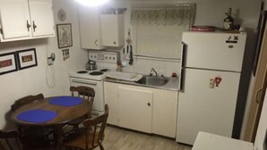 A compact kitchen with white cabinets, a stove, a sink, and a refrigerator. There is a dining table with chairs and a window with blinds. - Diamond in the Bluff (Pointe-du-Chene)
