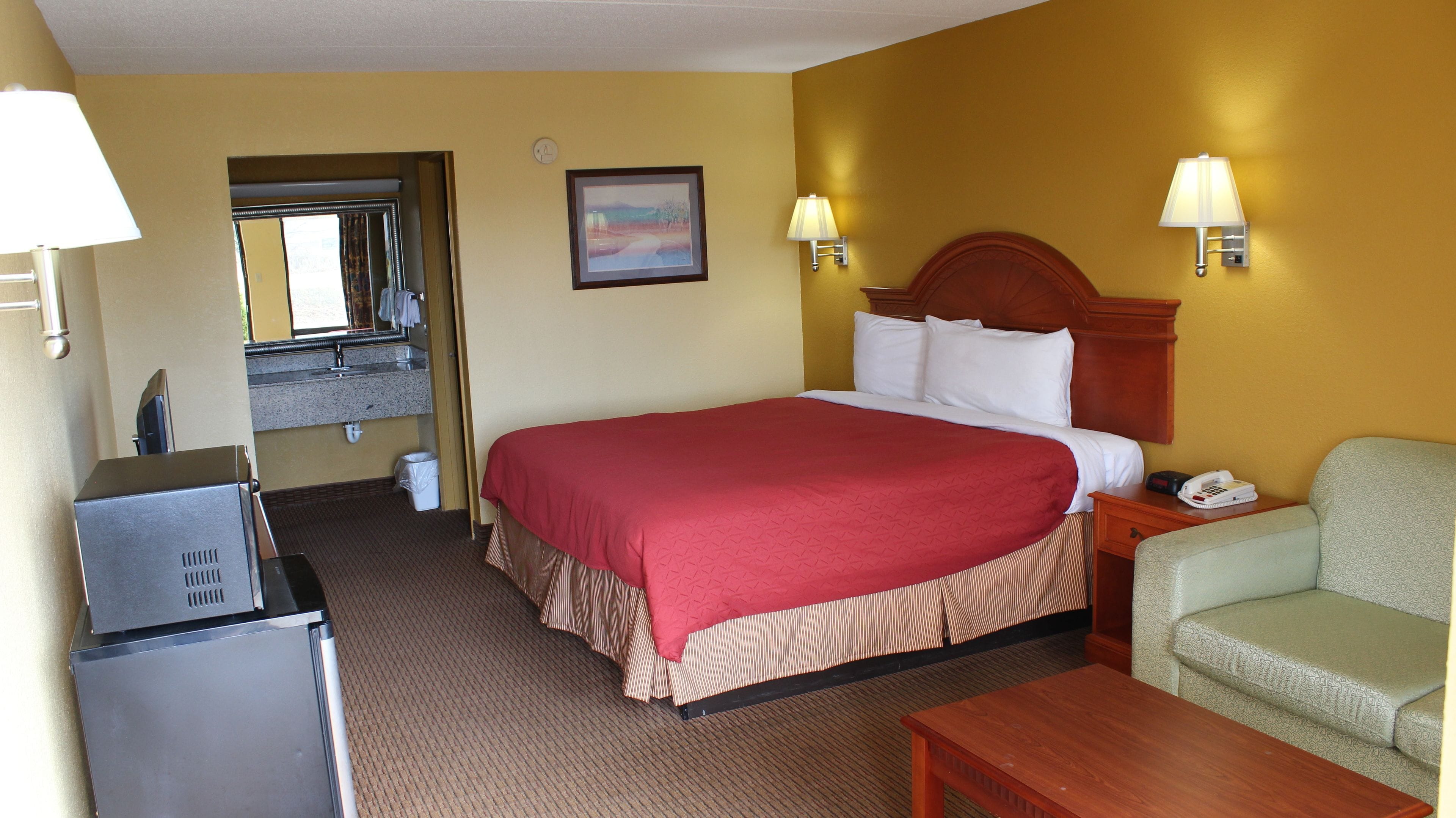 A hotel room with a large bed, a desk, a chair, a lamp, a telephone, and a picture on the wall.