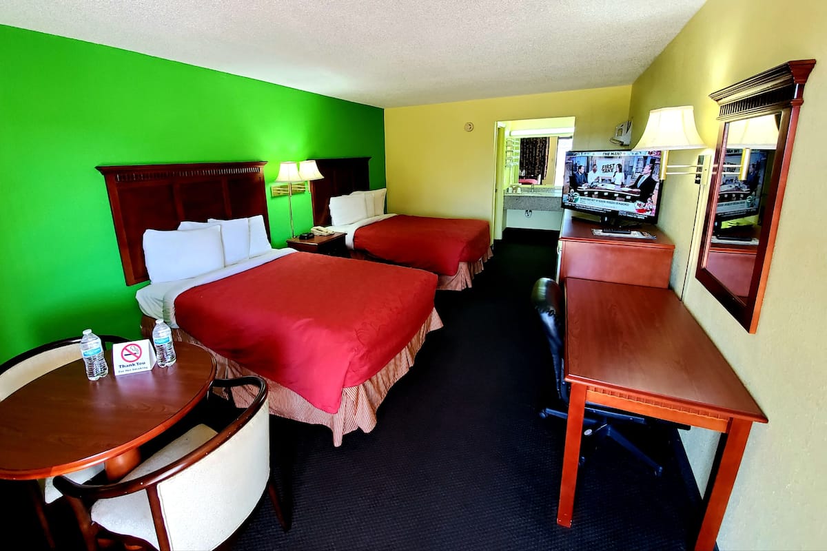Ein Hotelzimmer mit zwei Betten, einem Schreibtisch, einem Stuhl, einem Fernseher und einem sichtbaren Badezimmer im Hintergrund.