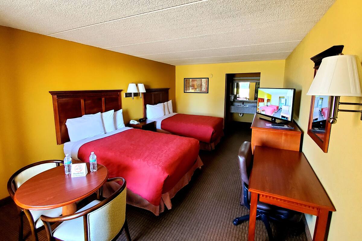 Ein Hotelzimmer mit zwei Betten, einem Schreibtisch, einem Stuhl, einem Fernseher und einer Schreibtischlampe.