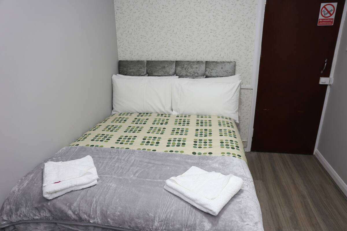 A hotel room with a bed, pillows, a no-smoking sign, and a folded towel on the bed.