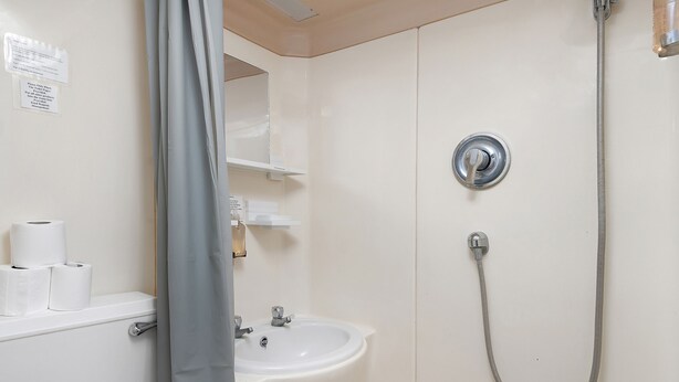 Un baño con lavamanos, inodoro y ducha. Hay rollos de papel higiénico en la encimera.