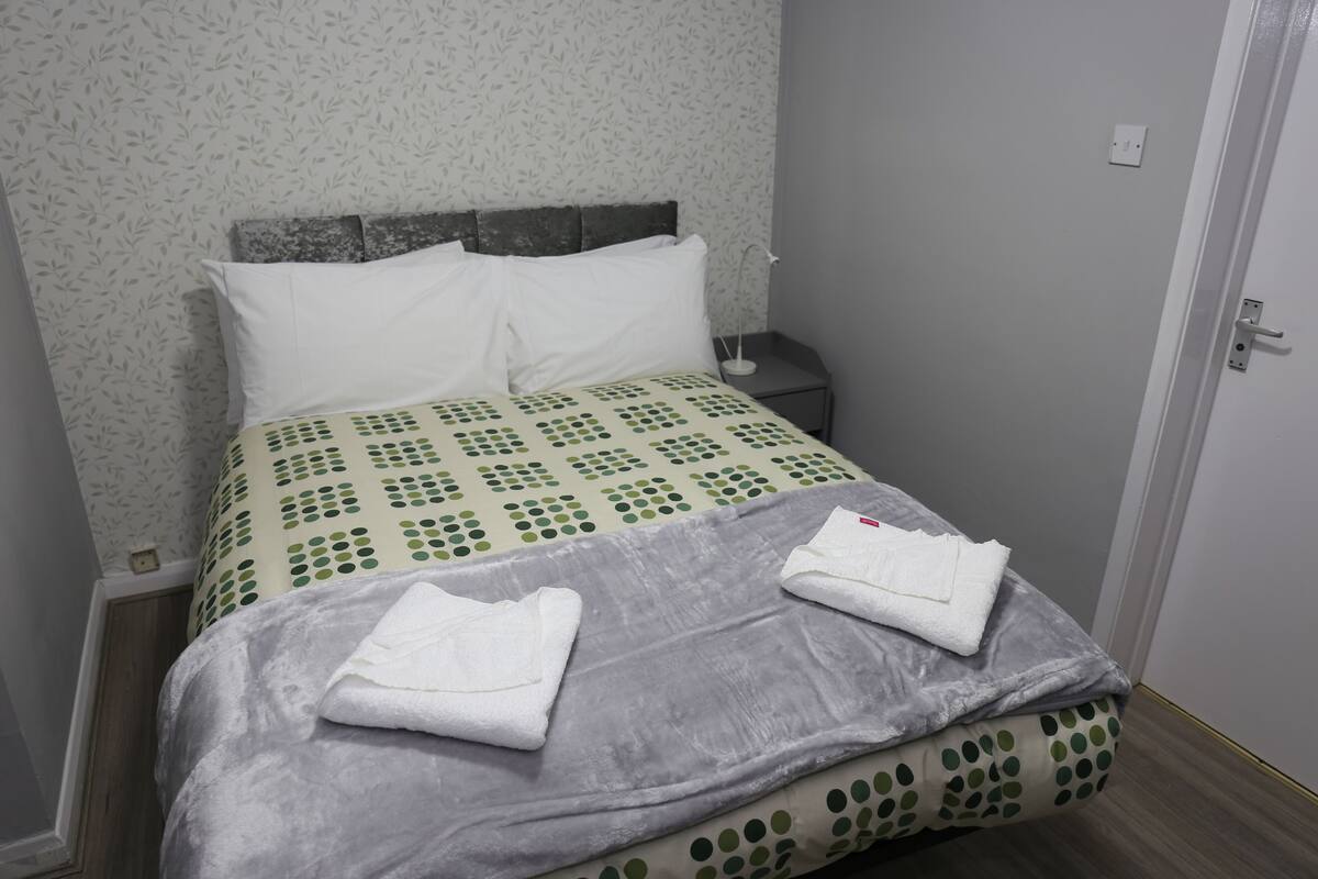 A neatly made bed with a patterned bedspread, pillows, and folded towels.