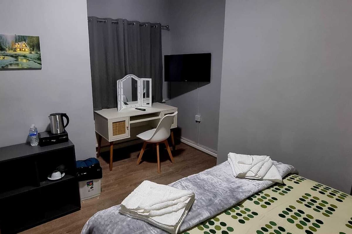 A hotel room with a bed, a desk with a chair, a small cabinet, a mirror, and a painting on the wall.