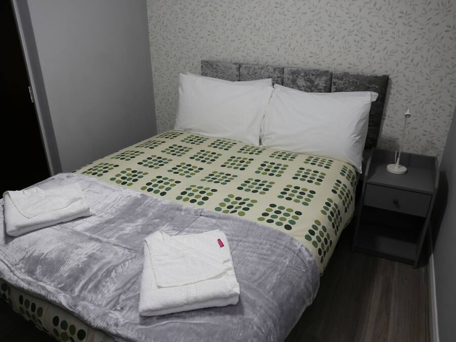 Una cama bien tendida con una colcha estampada, un cubrelecho gris y dos toallas blancas dobladas.