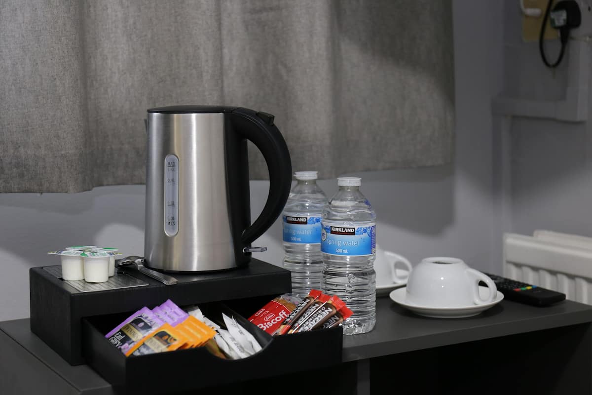 A hotel room with a coffee maker, two water bottles, a cup, and a remote control on a table.
