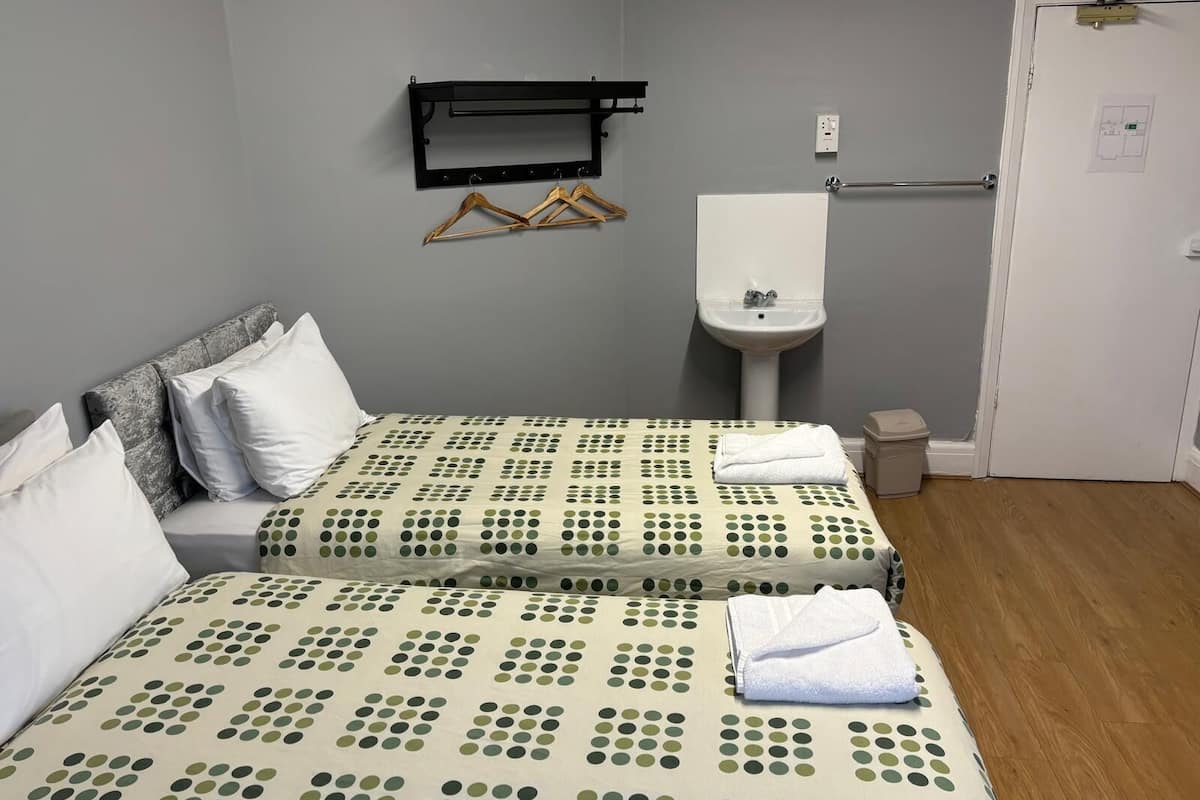 A room with two beds, a sink, a wardrobe, and a door.