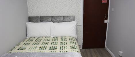 A neatly made bed with a patterned bedspread, a gray headboard, and white pillows. There is a door with a 'No Smoking' sign on it.