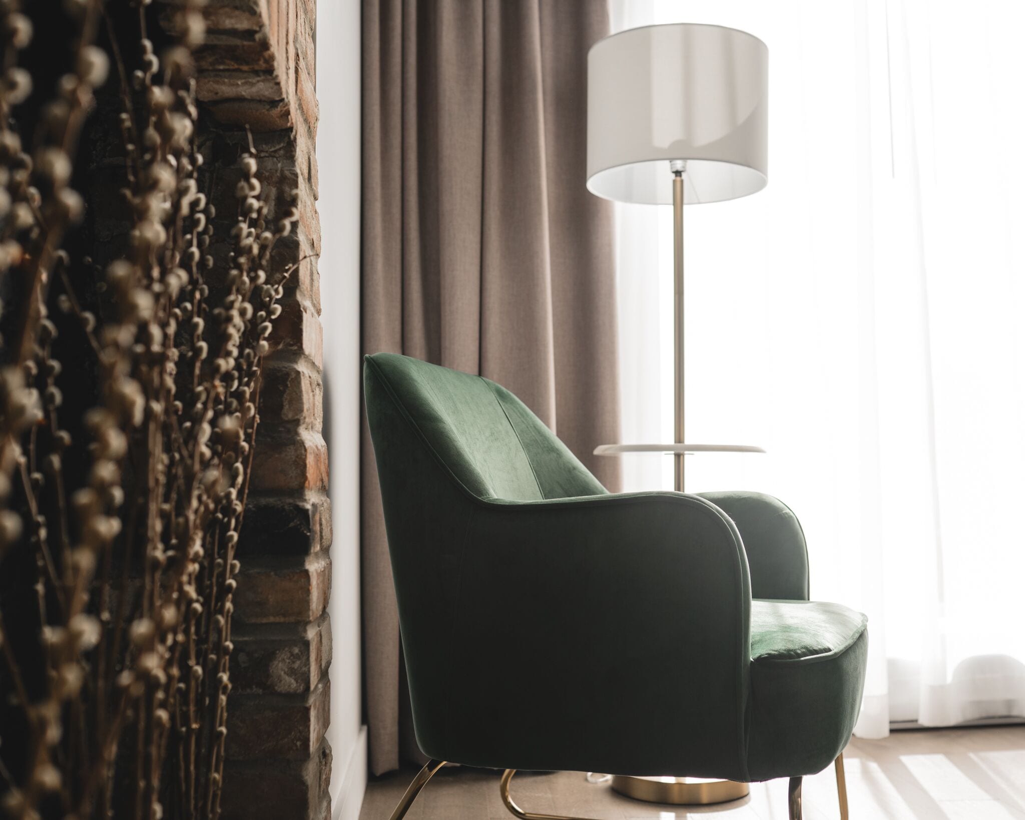 A room with a green upholstered chair, a floor lamp, and a curtain.